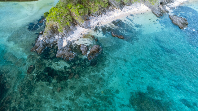 The serene seascape of Okinawa showcases crystal-clear waters, exposed rocky formations, and gentle waves lapping against the shore.