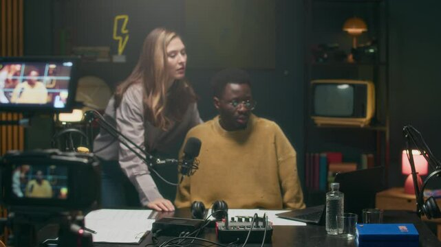 Medium long shot of young bicultural hosts checking equipment, doing soundcheck before podcast recording in modern studio