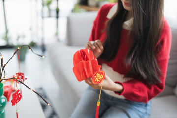 Asian Woman decorated house for Chinese New Year Celebrations. putting traditional pendant to the...