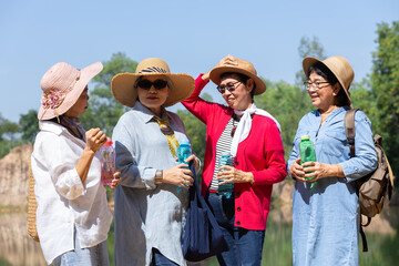 Group of retired elderly Asian women enjoy outdoor reunion traveling trip, casual clothing, smiling, holding water bottles, engaging in conversation, senior people surrounded by scenery sunny day