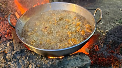 Hot oil bubbles furiously as food is frying in a large silver pan