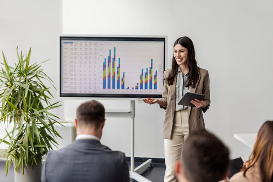 Young female data analyst standing at boardroom and having presentation on white board in front of managers.