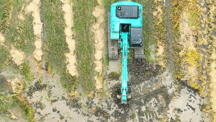 The view from above highlights the machine’s tracks as it moves through the rice field, reflecting the efficiency and power of modern machinery in agricultural practices.