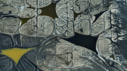 Visible tears in the waste pond lining highlight pollution risks from exposed industrial residues,...