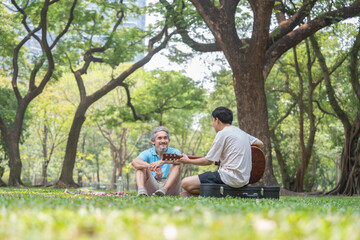 senior father and young adult son spend holiday time having picnic together,playing guitar,resting,conversation,concept family lifestyle,bonding,relationship