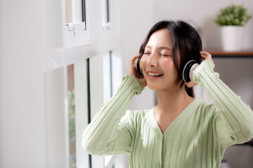 Portrait happy young woman wearing headphones listening music while standing with fun and enjoy in...