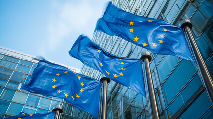European Union flags waving in front of a modern glass building under a clear blue sky.

