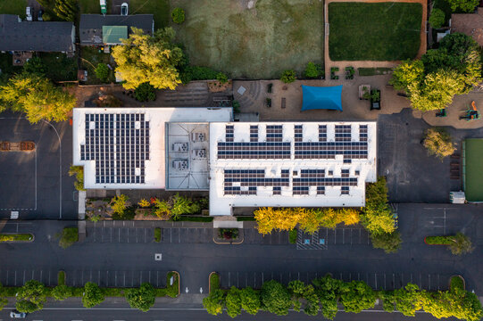 Aerial drone picture of a modern educational building in Beaverton, Oregon, showing large rooftop solar panels and HVAC units. Captured at sunset, emphasizing clean energy and sustainable design