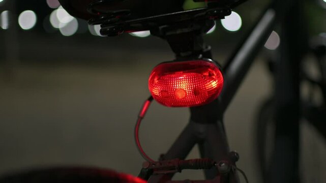 Pan camera movement around a back side of a bicycle with a blinking red light at night. Selective focus, nice blurry background.