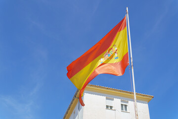 Spanish flag waving in the wind over a white building on a sunny day