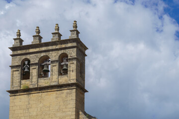 stone Belfry with three bells showing under cloudy sky
