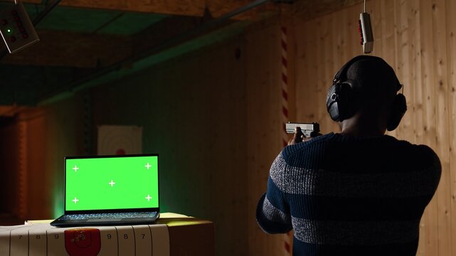 Chroma key notebook and shooting range customer reloading pistol, shooting targets. Isolated screen laptop next to man at shooting ground facility loading pistol, wearing protection goggles, camera A