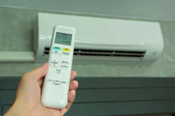 Man's hand using remote control open The air conditioner is cooled to 25 degrees Celsius in his bedroom. Health concepts and energy savings