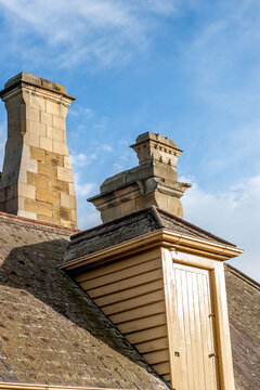 A dormer doorway in a slate roof with two elegant sandstone chimneys