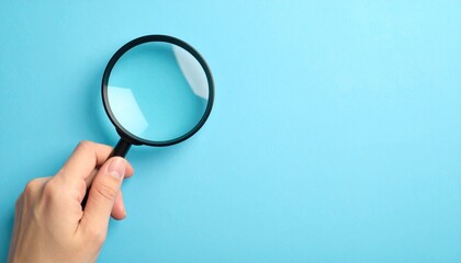 Close up photo of a hand holding a magnifying glass on a plain blue background