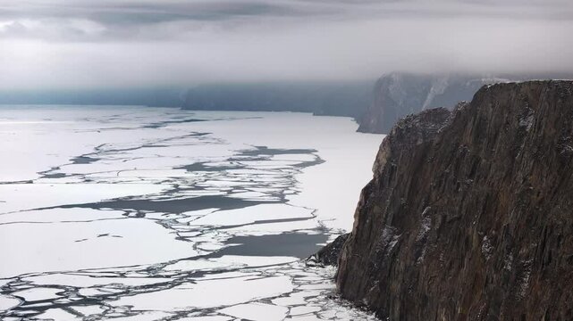 Aerial landscape view over sea ice floes, covered in snow, at overcast