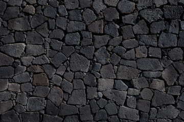 Close-up and frontal view of a rustic basalt stone wall with rough texture and organic pattern, ideal as architectural or design background.