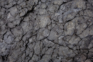Detailed close-up of fractured volcanic stone surface with natural crevices and layered textures,...