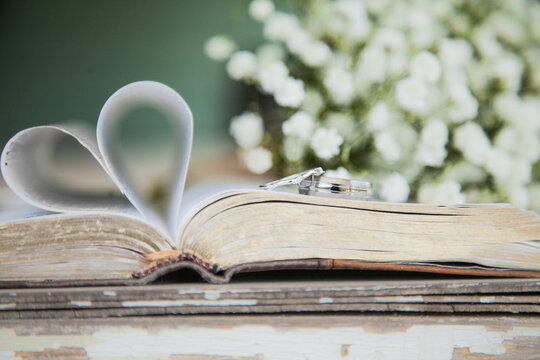 Silver bride and grooms wedding rings laid on the bible shaped in a heart