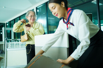 Elderly Asian female woman is proceeding baggage check-in at airline checkin counter in modern airport.