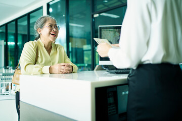 Elderly Asian female woman is proceeding baggage check-in at airline checkin counter in modern...