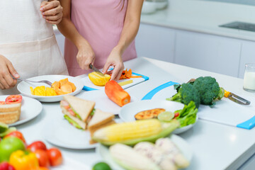 Asian couple, with the wife heavily pregnant, happily preparing food and peeling fruit together in the kitchen. 