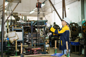 Caucasian female mechanical engineer inspecting and maintaining machinery inside a metalworking factory. 