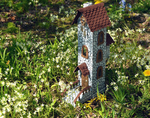 Cute fairy doll house or tower with spring flowers outside in the garden. Lovely miniature for greeting cards, wedding or birthday, real estate, downsizing, home ownership. Vintage spring background