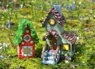 Cute fairy doll house with spring flowers outside in the garden. Lovely miniature for greeting cards, wedding or birthday concept, real estate, downsizing, home ownership. Vintage spring background