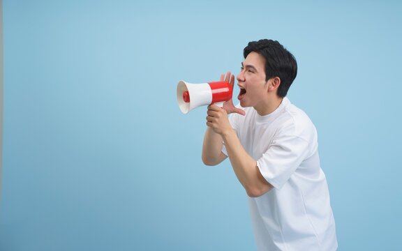 Young man enthusiastically speaks into megaphone while wearing a white shirt against a light blue background