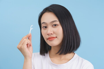Young woman demonstrating dental hygiene with a floss tool in a bright blue background setting...