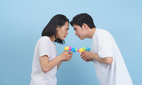 Playful standoff between two friends with water guns against a soft blue background