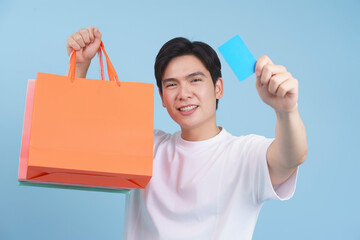 Young man happily holding shopping bags and a membership card against a blue background in a...
