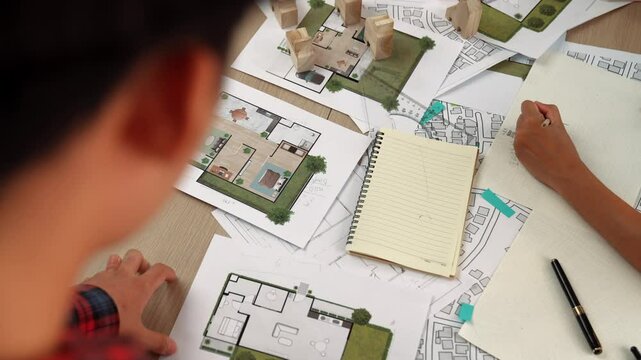 Architect and engineer consider or discuss about building construction using blueprint on table with architectural document, measurement tool and wooden block scatter around at office. Delineation.