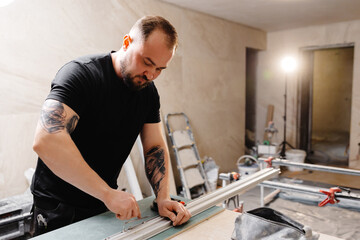 Construction worker cutting aluminum profiles for installing stretch ceiling