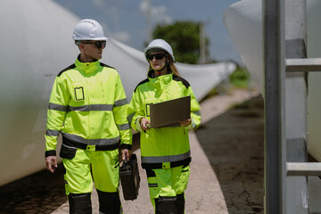 Maintenance engineer team standing at windmills at wind turbine farm. Group of people wear safety...