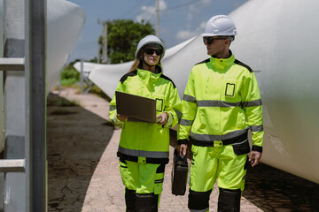 Maintenance engineer team standing at windmills at wind turbine farm. Group of people wear safety helmet and uniform working at alternative renewable energy wind station. Sustainable energy technology