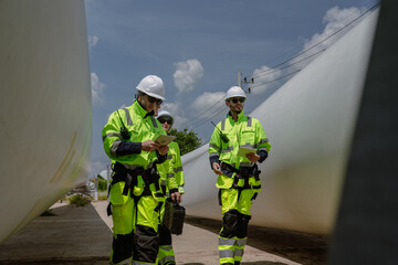 Maintenance engineer team standing at windmills at wind turbine farm. Group of people wear safety...