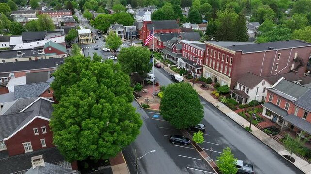 Patriotic American flag waves over small town in USA. Main Street in Small Town America square at cloudy day in spring. Aerial Approaching shot. Manheim, Pennsylvanias.
