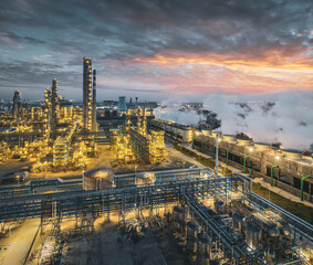 Aerial view of a large oil refinery and chemical plant complex illuminated at dusk with dramatic...