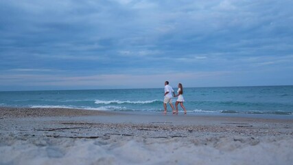 A happy couple is running on the sand near the ocean and admiring each other