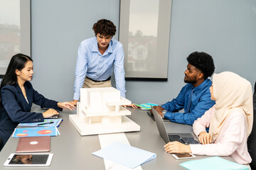 Architects and designers work presenting and discussing house model in office meeting. The participants are engaged in an in-depth conversation, Experts look at model homes and architectural drawings