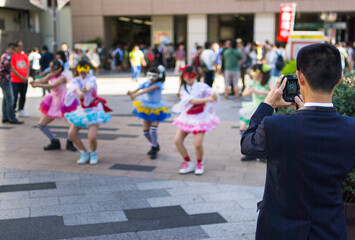Businessman taking a photo of a Japanese girl group performing a routine outside Akihabara station in Tokyo.