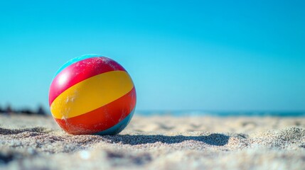 Obraz premium A close-up of a colorful beach ball with vibrant stripes, lying on the sand with a clear blue sky in the background, capturing a sunny summer day.