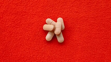Bunch of medicine pills or drugs isolated on red table background with copy space. Medical insurance, health disparities and high treatment cost concept. Extreme closeup rotating top view.