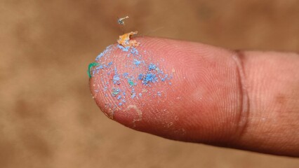 Toxic microplastic particle pieces or fragments on finger tip. Closeup macro top view. Micro or macro plastic pollution or contamination problem concept.