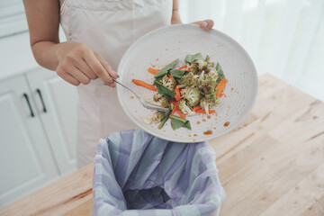 Woman in kitchen sorting organic waste into recycling bin, promoting sustainability, zero waste...