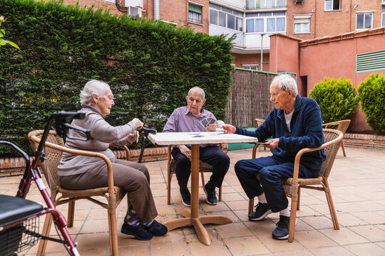 Elderly individuals engage in a card game at an outdoor table in a nursing home courtyard, fostering social interaction and relaxation