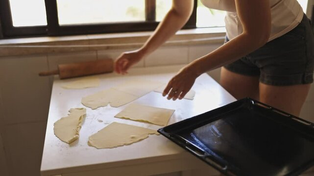 Woman arranging puff pastry on baking sheet in kitchen