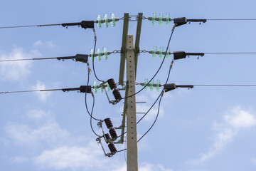Power lines and insulators on a concrete pole against blue sky